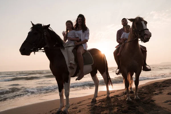 The family spends time with their children while riding horses together on a sandy beach. Selective focus — стоковое фото