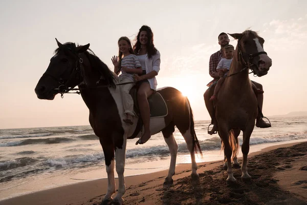 The family spends time with their children while riding horses together on a sandy beach. Selective focus — Zdjęcie stockowe