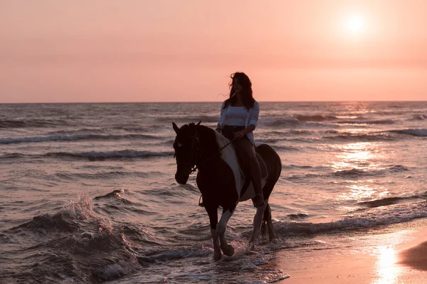 Женщина в летней одежде любит кататься на лошади на прекрасном песчаном пляже на закате. Селективный фокус — стоковое фото
