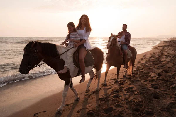 The family spends time with their children while riding horses together on a sandy beach. Selective focus — Zdjęcie stockowe