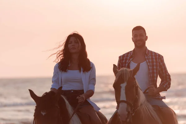 A loving couple in summer clothes riding a horse on a sandy beach at sunset. Sea and sunset in the background. Selective focus — Foto Stock