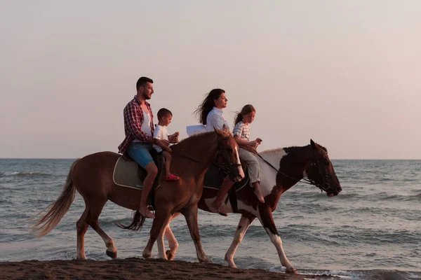 The family spends time with their children while riding horses together on a sandy beach. Selective focus —  Fotos de Stock
