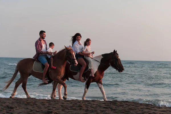 The family spends time with their children while riding horses together on a sandy beach. Selective focus — Stok fotoğraf