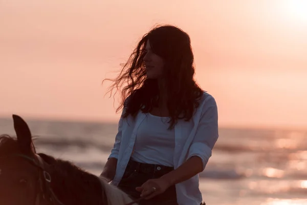 Mujer en ropa de verano disfruta montar a caballo en una hermosa playa de arena al atardecer. Enfoque selectivo — Foto de Stock