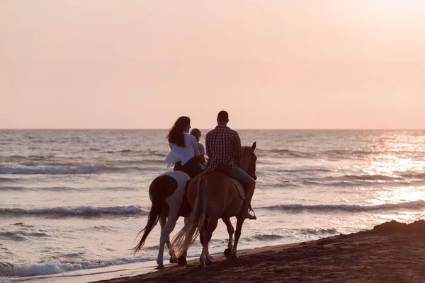 The family spends time with their children while riding horses together on a sandy beach. Selective focus — Stock fotografie