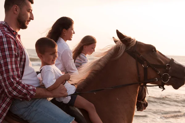 The family spends time with their children while riding horses together on a sandy beach. Selective focus — Stok fotoğraf