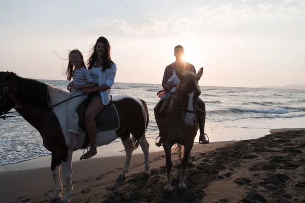 The family spends time with their children while riding horses together on a sandy beach. Selective focus — Stock Photo, Image