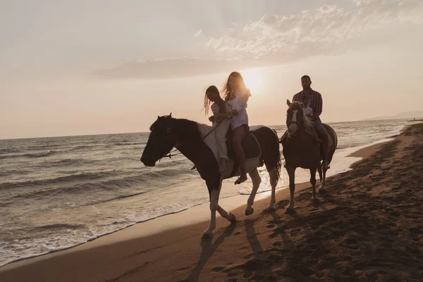 The family spends time with their children while riding horses together on a sandy beach. Selective focus — Zdjęcie stockowe