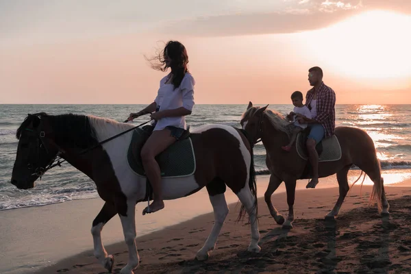 Aile kumlu bir sahilde birlikte ata binerken çocuklarıyla vakit geçirir. Seçici odak 