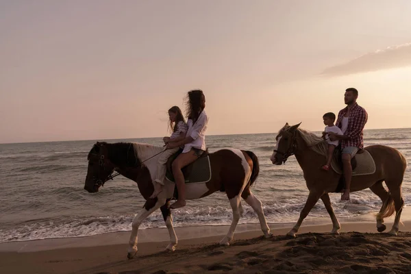 The family spends time with their children while riding horses together on a sandy beach. Selective focus — 스톡 사진