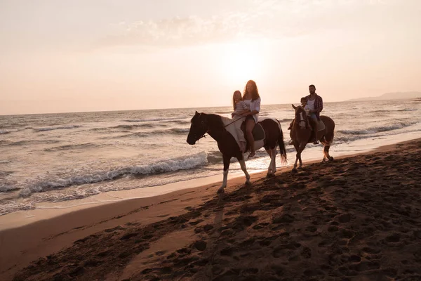 The family spends time with their children while riding horses together on a sandy beach. Selective focus — 图库照片