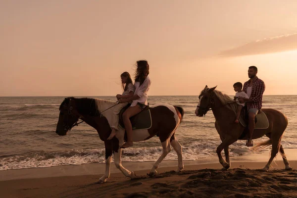 A família passa tempo com seus filhos enquanto montam cavalos juntos em uma praia de areia. Foco seletivo — Fotografia de Stock