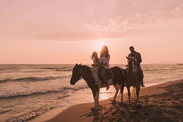 The family spends time with their children while riding horses together on a sandy beach. Selective focus — 스톡 사진