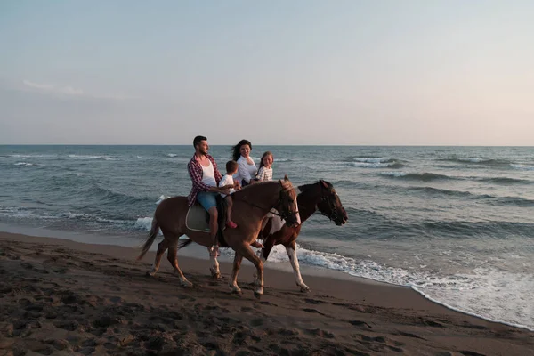 The family spends time with their children while riding horses together on a sandy beach. Selective focus — Stock fotografie