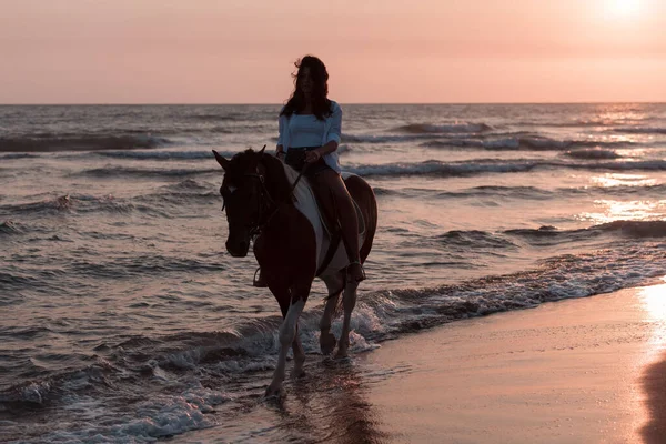Yaz kıyafetleri içinde bir kadın gün batımında kumlu güzel bir sahilde ata binmekten hoşlanır. Seçici odak 