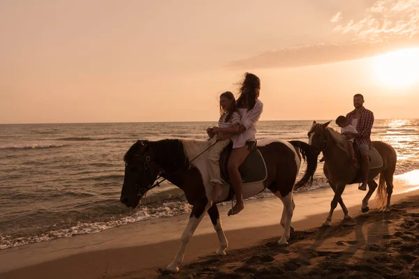 The family spends time with their children while riding horses together on a sandy beach. Selective focus — стоковое фото