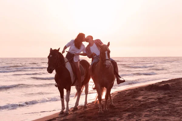 A loving couple in summer clothes riding a horse on a sandy beach at sunset. Sea and sunset in the background. Selective focus Stock Image