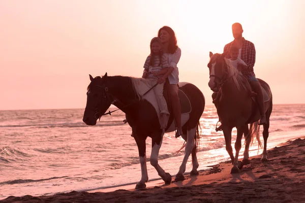 The family spends time with their children while riding horses together on a sandy beach. Selective focus Stock Photo