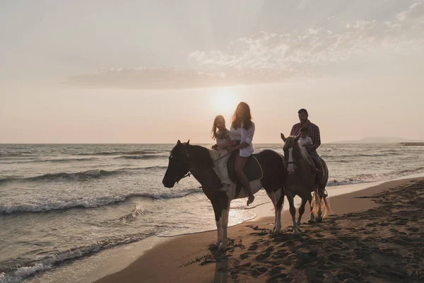 The family spends time with their children while riding horses together on a beautiful sandy beach on sunet. — 图库照片