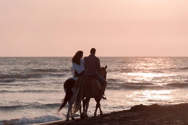 The family spends time with their children while riding horses together on a beautiful sandy beach on sunet. — Zdjęcie stockowe