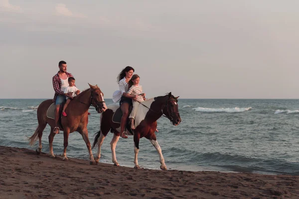 The family spends time with their children while riding horses together on a beautiful sandy beach on sunet. — 스톡 사진