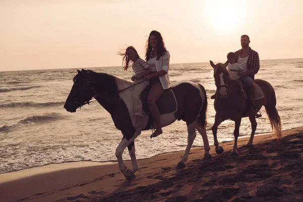 The family spends time with their children while riding horses together on a beautiful sandy beach on sunet. — Foto Stock