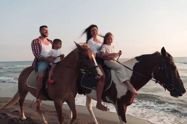 Семья проводит время со своими детьми, катаясь на лошадях вместе на красивом песчаном пляже на солнце. — стоковое фото