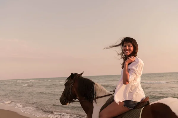 Frau in Sommerkleidung genießt es, bei Sonnenuntergang auf einem Pferd an einem schönen Sandstrand zu reiten. Selektiver Fokus — Stockfoto