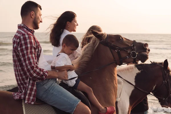 The family spends time with their children while riding horses together on a beautiful sandy beach on sunet. — Stok fotoğraf