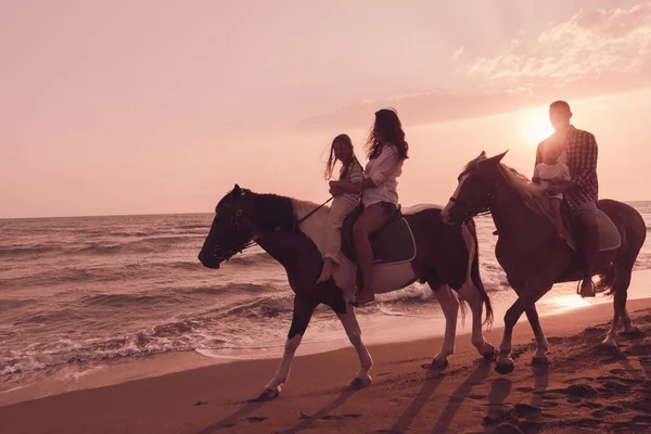 家族は日没の美しい砂浜で一緒に馬に乗っている間、子供たちと一緒に時間を過ごします. — ストック写真