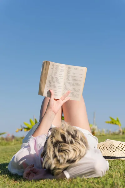 在阳光明媚的夏天或春日，女人躺在绿草覆盖的草地上看书. — 图库照片