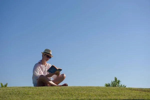 Mulher deitada e lendo seu livro favorito em um prado coberto com grama verde fresca em um verão ensolarado ou dia de primavera. — Fotografia de Stock