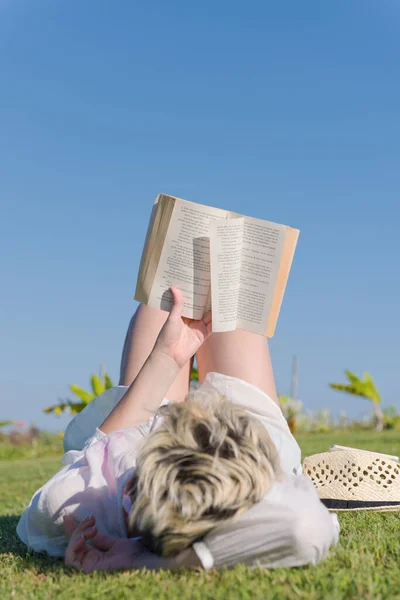 Γυναίκα ξαπλωμένη και διαβάζοντας το αγαπημένο της βιβλίο σε ένα λιβάδι καλυμμένο με φρέσκο πράσινο γρασίδι σε ένα ηλιόλουστο καλοκαίρι ή την άνοιξη ημέρα. — Φωτογραφία Αρχείου