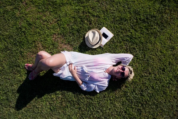 Horní pohled shora na ženu ležící a odpočívající na louce pokryté zelenou trávou za slunečného léta nebo jarního dne. — Stock fotografie