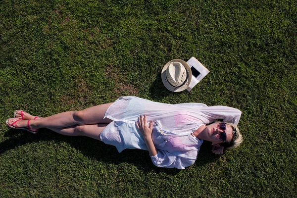 Vue de dessus d'une femme allongée et relaxante sur une prairie couverte d'herbe verte par une journée ensoleillée d'été ou de printemps. — Photo