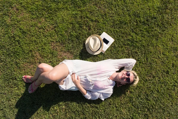 夏や春の日に緑の芝生に覆われた草原に横たわってリラックスした女性の上からのトップビュー. — ストック写真