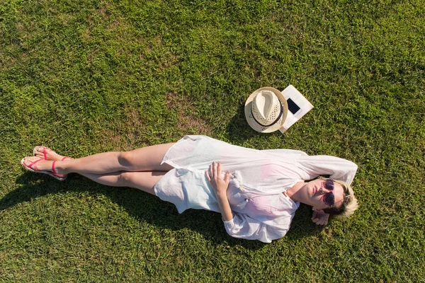 Ovanifrån av en kvinna liggande och avkopplande på en äng täckt med grönt gräs en solig sommar eller vår dag. — Stockfoto