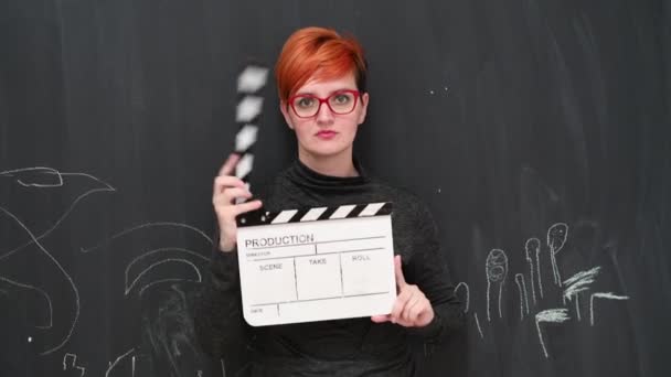 Redhair vrouw actrice poseren met film clapper boord glimlachen en kijken naar camera tegen krijtbord achtergrond. — Stockvideo