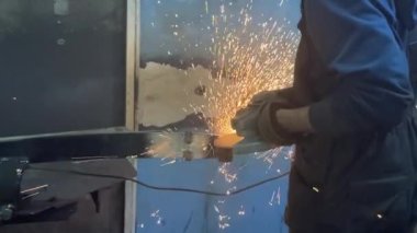 Adam dairesel testere ile çalışıyor. Sıcak metalden kıvılcımlar çıkıyor. Adam çeliğin üzerinde çok çalıştı. Garajın karanlık arka planında yavaş çekim yakın çekim