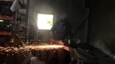 Adam dairesel testere ile çalışıyor. Sıcak metalden kıvılcımlar çıkıyor. Adam çeliğin üzerinde çok çalıştı. Garajın karanlık arka planında yavaş çekim yakın çekim