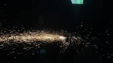 Adam dairesel testere ile çalışıyor. Sıcak metalden kıvılcımlar çıkıyor. Adam çeliğin üzerinde çok çalıştı. Garajın karanlık arka planında yavaş çekim yakın çekim