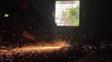 Adam dairesel testere ile çalışıyor. Sıcak metalden kıvılcımlar çıkıyor. Adam çeliğin üzerinde çok çalıştı. Garajın karanlık arka planında yavaş çekim yakın çekim