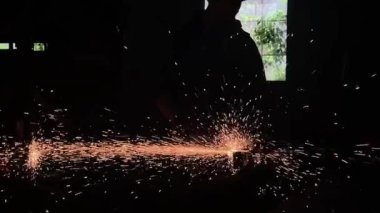 Adam dairesel testere ile çalışıyor. Sıcak metalden kıvılcımlar çıkıyor. Adam çeliğin üzerinde çok çalıştı. Garajın karanlık arka planında yavaş çekim yakın çekim