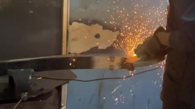 Adam dairesel testere ile çalışıyor. Sıcak metalden kıvılcımlar çıkıyor. Adam çeliğin üzerinde çok çalıştı. Garajın karanlık arka planında yavaş çekim yakın çekim