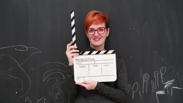 Ryšavý žena herečka pózuje s filmem tleskání palubě s úsměvem a při pohledu na kameru proti tabuli pozadí. — Stock video