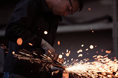 Heavy Industry Engineering Factory Interior with Industrial Worker Using Angle Grinder and Cutting a Metal Tube. Güvenlik Üniforması ve Sert Şapka Üretim Metal Yapıları Müteahhiti. Yüksek kalite