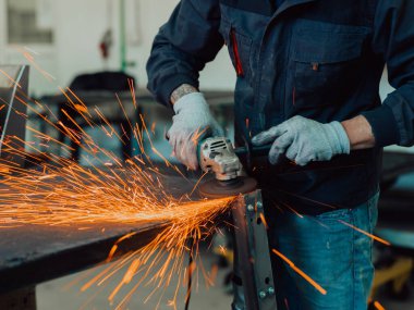 Heavy Industry Engineering Factory Interior with Industrial Worker Using Angle Grinder and Cutting a Metal Tube. Güvenlik Üniforması ve Sert Şapka Üretim Metal Yapıları Müteahhiti. Yüksek kalite