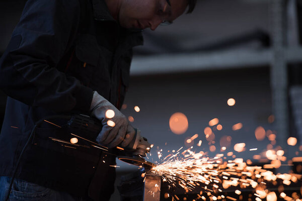Heavy Industry Engineering Factory Interior with Industrial Worker Using Angle Grinder and Cutting a Metal Tube. Contractor in Safety Uniform and Hard Hat Manufacturing Metal Structures. High-quality