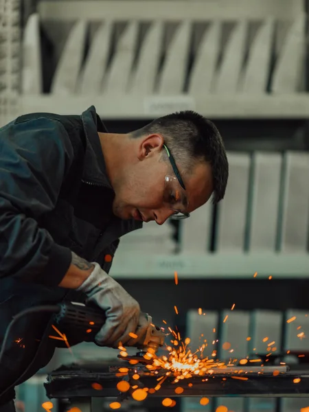 Heavy Industry Engineering Factory Interior with Industrial Worker Using Angle Grinder and Cutting a Metal Tube. Contractor in Safety Uniform and Hard Hat Manufacturing Metal Structures. High-quality