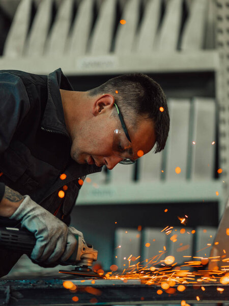 Heavy Industry Engineering Factory Interior with Industrial Worker Using Angle Grinder and Cutting a Metal Tube. Contractor in Safety Uniform and Hard Hat Manufacturing Metal Structures. High-quality